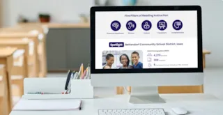 Computer screen shows five reading skills and Bettendorf school district info; classroom and desk supplies are visible.