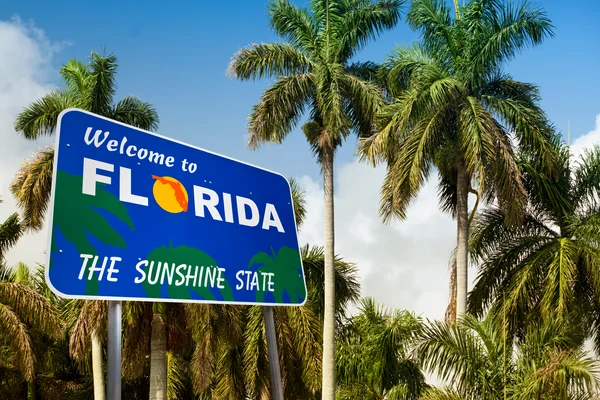 A Welcome to Florida sign with palm trees and a blue sky in the background.