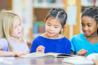 Three children read a book together in a library
