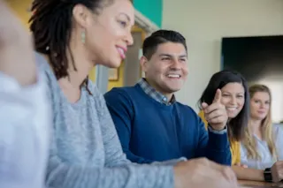 Four people sit at a table in a meeting, smiling and engaged in conversation, with one man gesturing.