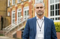 A male principal standing outdoors on school grounds