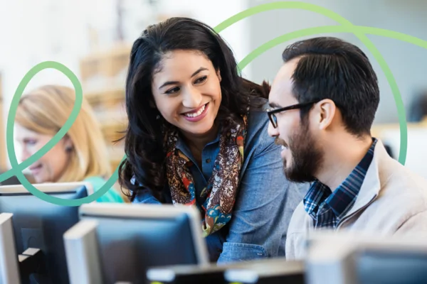 Two people smiling and talking at computers, with a woman working in the background and green swirls overlayed.