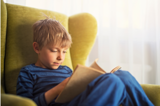 A child reclines in an armchair, absorbed in a book