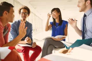 Four teachers sit in a circle, smiling and sharing ideas