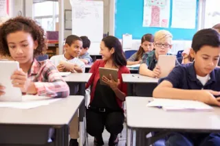 Students read on tablets while a teacher smiles at a student.