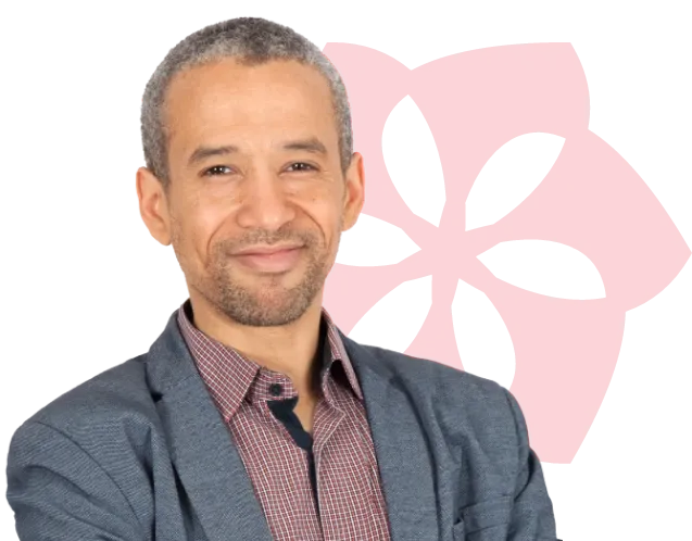 Smiling man in a blazer stands in front of a red floral pattern.