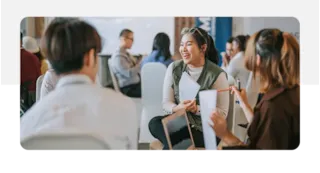 Group of people engaged in a lively discussion, with one woman smiling and holding papers.