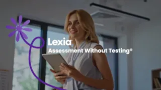 Teacher helping a student with a tablet in a classroom, while other students work in the background.