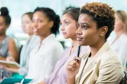 Several women sit in a row, attentively listening and taking notes during a seminar or workshop.