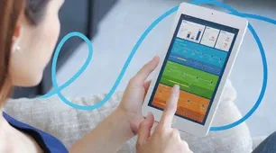 A person uses a tablet displaying colorful charts and data while sitting on a couch.