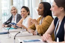 A group of administrators sit smiling at a table in front of microphones.