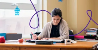 A woman sits at a desk writing in a notebook.