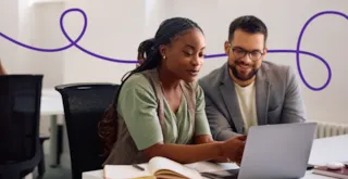 A woman and a man in an office looking at a laptop together.