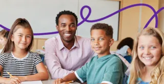A teacher smiling alongside three students at a classroom table.