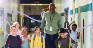 A teacher walks down a school hallway with five students.