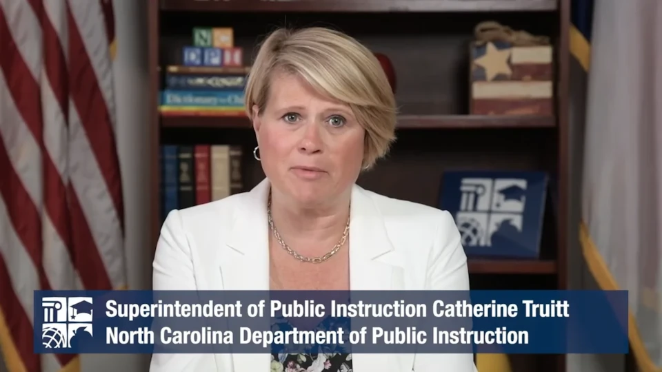 Woman in a white blazer speaks in front of bookshelves; text reads Superintendent of Public Instruction Catherine Truitt.