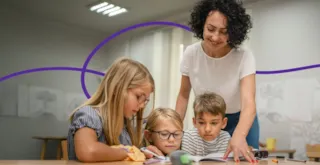 A teacher helps three young students with schoolwork at a desk in a classroom.