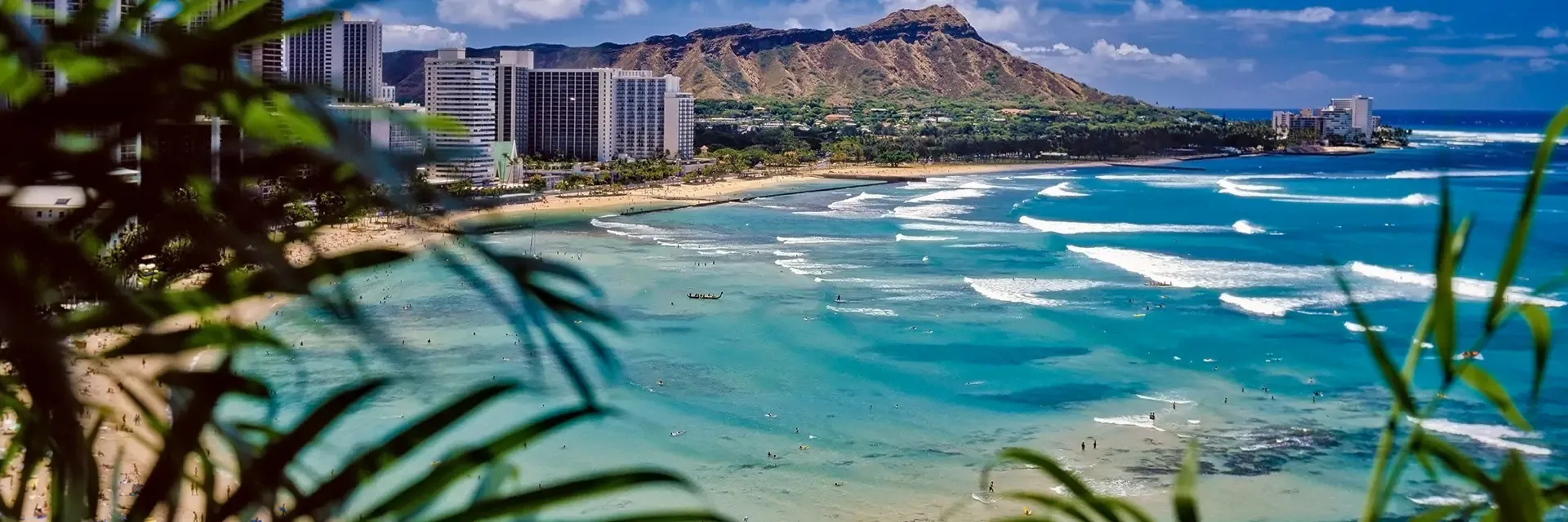 A view of Waikiki Beach with turquoise water, city buildings, and Diamond Head crater in the background.