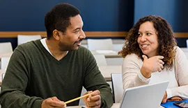 Two teachers converse with smiles while sitting at a desk