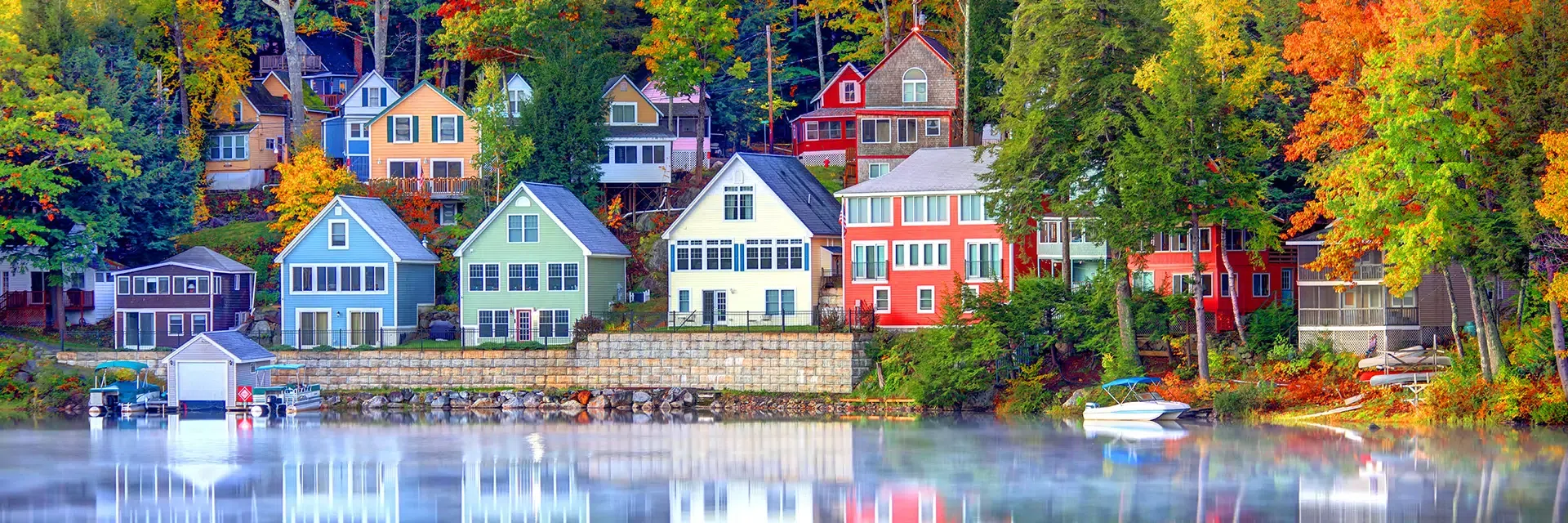 Colorful lakeside houses surrounded by autumn trees, their reflections visible in the calm water below.