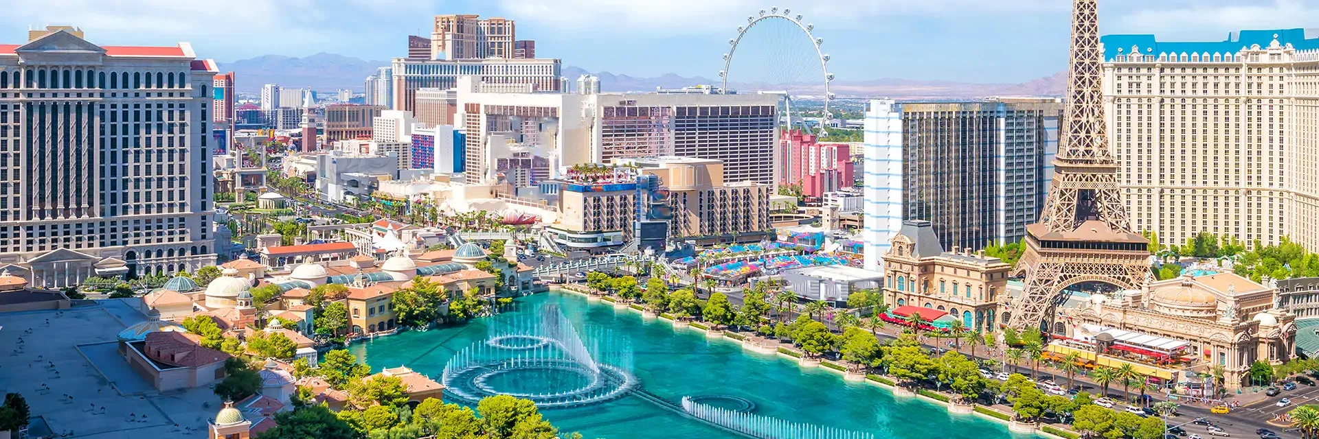 Aerial view of the Las Vegas Strip with hotels, casinos, and a large fountain in the foreground under a clear sky.