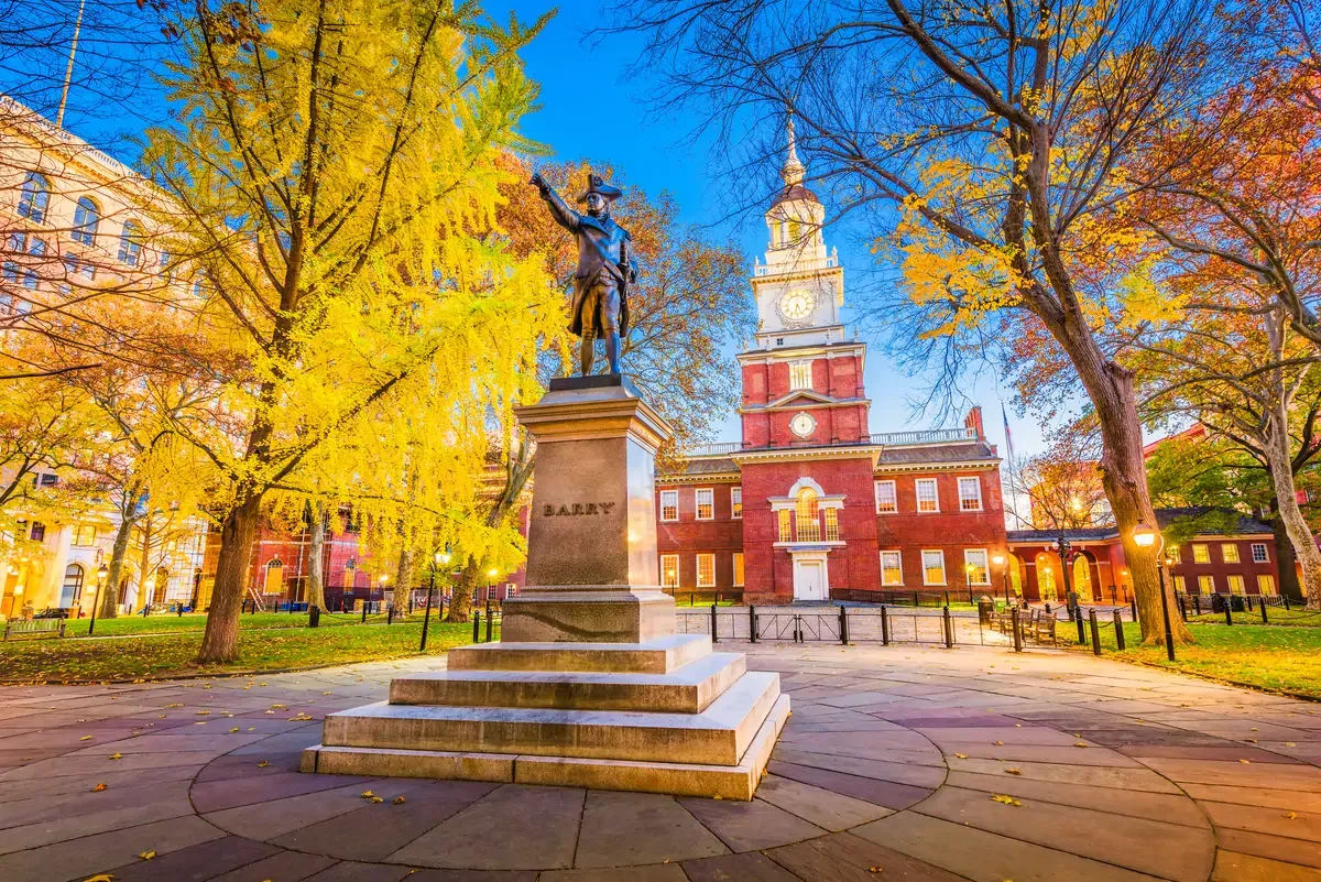 Statue of Commodore Barry in front of Independence Hall surrounded by trees at dusk in Philadelphia.