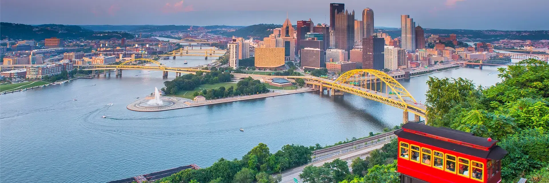 A red and yellow incline car overlooking Pittsburgh’s skyline, rivers, and yellow bridges at sunset.