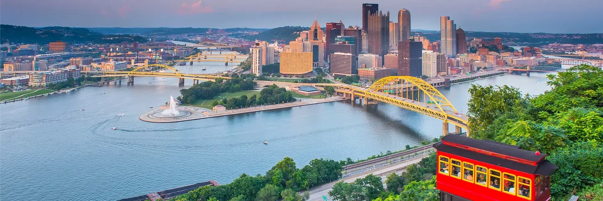 City skyline with yellow bridges over rivers, a fountain, and a red incline car in the foreground, Pittsburgh, PA.