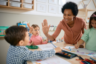 A teacher high-fives a young student in a classroom