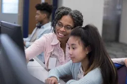 A teacher and student smiling and working together at a computer in a classroom.