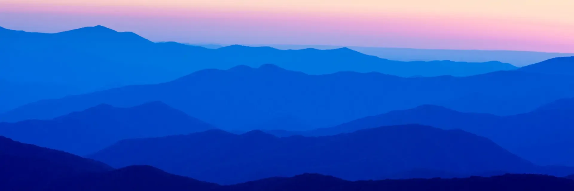 Blue Ridge mountains in layers at sunrise with a pink and orange gradient sky above.
