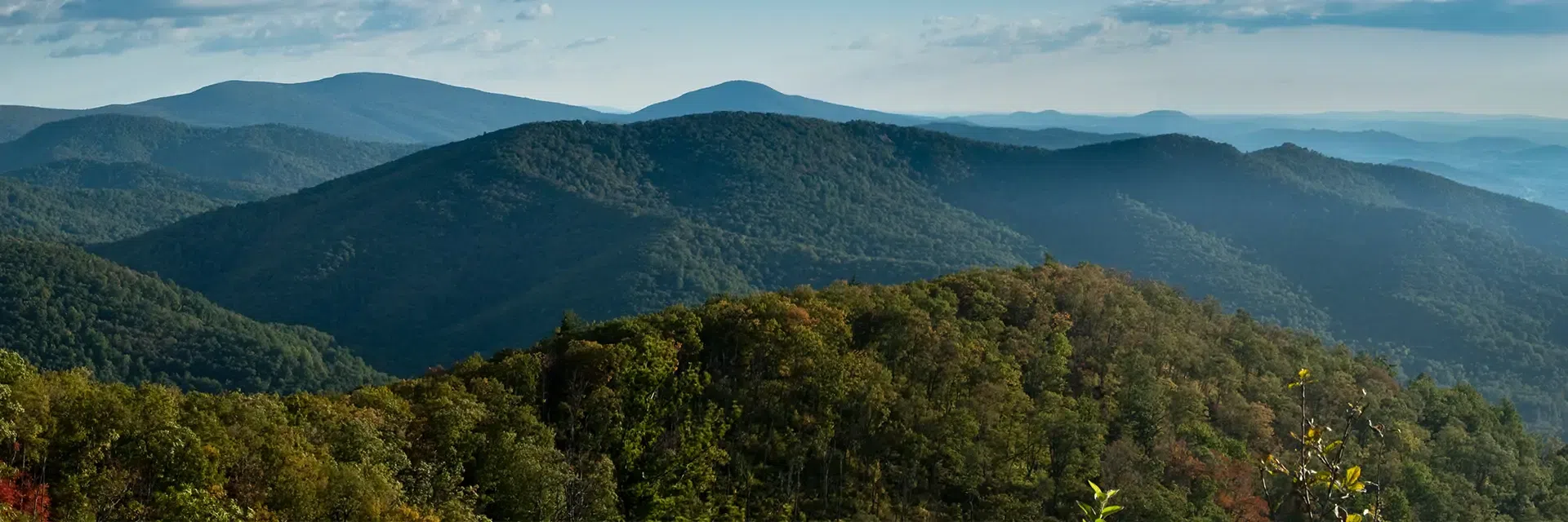 Rolling green mountains under a blue sky with scattered clouds, viewed from an elevated vantage point.