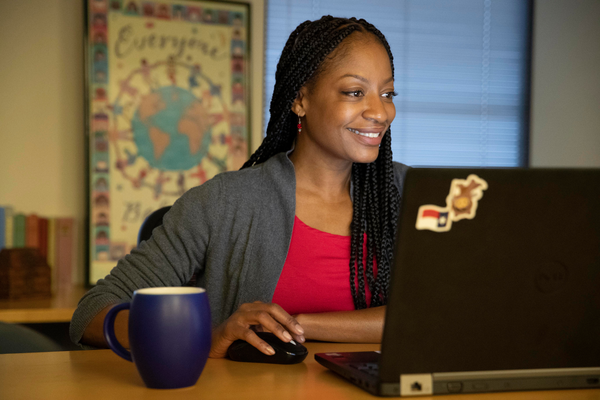 A woman sits at a desk in front of her computer with a coffee mug in front of her